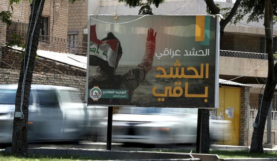 In this Tuesday, July 2, 2019, photo, motorists pass by a Popular Mobilization poster in Baghdad, Iraq. The Iraqi government&#39;s move to place Iranian-backed militias under the command of the armed forces is a political gamble by a prime minister increasingly caught in the middle of a dangerous rivalry between Iran and the U.S., the two main power brokers in Iraq. (AP Photo/Hadi Mizban)