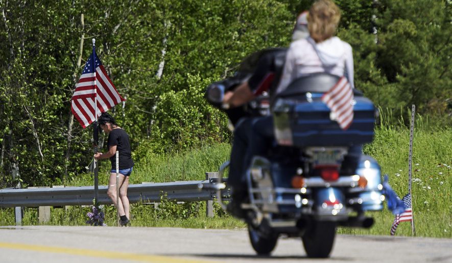 In this June 22, 2019 file photo, a motorcycle passes as a woman leaves flowers at the scene of an accident on Route 2 in Randolph, N.H., where seven motorcyclists were killed in a crash the day before. Hundreds of bikers are expected to converge on Randolph on Saturday, July 6, to remember the seven riders who were killed. The pickup driver who collided with them has been charged in the crash. (Paul Hayes/Caledonian-Record via AP, File)