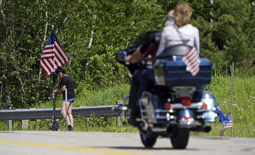 In this June 22, 2019 file photo, a motorcycle passes as a woman leaves flowers at the scene of an accident on Route 2 in Randolph, N.H., where seven motorcyclists were killed in a crash the day before. Hundreds of bikers are expected to converge on Randolph on Saturday, July 6, to remember the seven riders who were killed. The pickup driver who collided with them has been charged in the crash. (Paul Hayes/Caledonian-Record via AP, File)