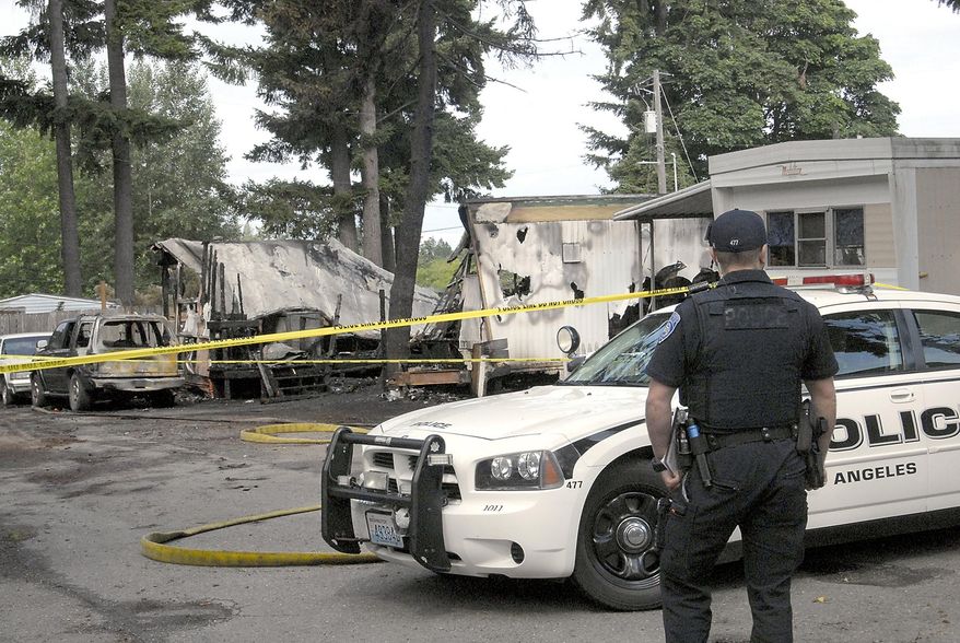 Port Angeles police Officer T.J. Mueller looks over the scene of a fire that destroyed two mobile homes and left several dead early Saturday, July 6, 2019, at the Welcome Inn RV Park in Port Angeles, Wash. Multiple people are believed to be dead following a fire at a mobile home park site in western Washington. The Peninsula Daily News reports the fire at the Welcome Inn RV Park in west Port Angeles broke out about 2:30 a.m. Saturday. (Keith Thorpe/The Peninsula Daily News via AP)