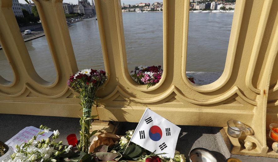 FILE - In this Saturday, June 1, 2019 file photo, flowers and flag of South Korea are laid on the Margit Bridge where a sightseeing boat capsized in Budapest, Hungary. Hungarian police say a South Korean woman recovered from the Danube River has been identified as the 27th fatality of the May 29 crash between a tour boat and a cruise ship. Police said Saturday, July 6 that the body was found some 58 kilometers (36 miles) downstream from the scene of the accident at Budapest's Margit Bridge. (AP Photo/Laszlo Balogh, file)