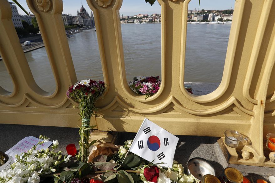 FILE - In this Saturday, June 1, 2019 file photo, flowers and flag of South Korea are laid on the Margit Bridge where a sightseeing boat capsized in Budapest, Hungary. Hungarian police say a South Korean woman recovered from the Danube River has been identified as the 27th fatality of the May 29 crash between a tour boat and a cruise ship. Police said Saturday, July 6 that the body was found some 58 kilometers (36 miles) downstream from the scene of the accident at Budapest's Margit Bridge. (AP Photo/Laszlo Balogh, file)