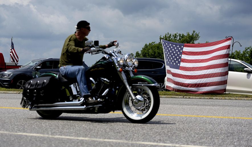 A motorcyclist passes an American flag on the route for the Ride for the Fallen 7 in near Randolph, N.H., on Saturday, July 6, 2019. Thousands of motorcyclists traveled through parts of New Hampshire as a tribute to the seven bikers killed in a collision with a pickup truck last month. (Paul Hayes/Caledonian-Record via AP)
