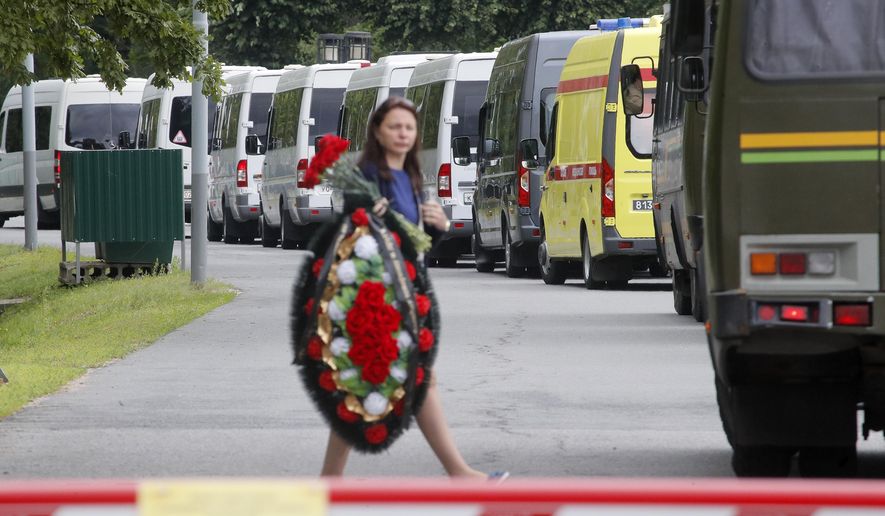 A woman carries a wreath as buses with bodies of the 14 crew members who died in a fire on a Russian navy's deep-sea research submersible, drive to the Serafimovskoye memorial cemetery during a funeral ceremony in St. Petersburg, Russia, Saturday, July 6, 2019. Russian President Vladimir Putin has awarded the nation's highest honors to 14 seamen who died in a fire on one of the navy's research submersibles. (AP Photo/Dmitri Lovetsky)