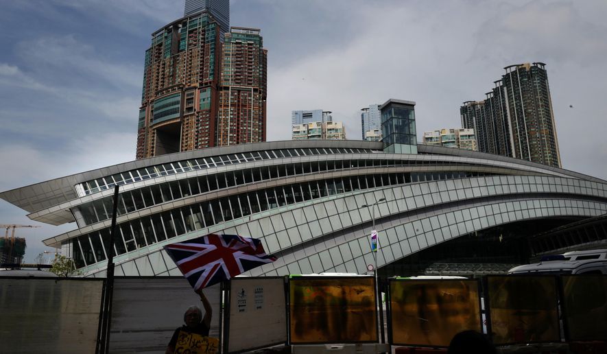 FILE - In this Sept. 22, 2018, file photo, a woman waves a British flag outside the Western Kowloon Station during a protest against the opening ceremony of the Hong Kong Express Rail Link in Hong Kong. Protesters in Hong Kong have chosen the new high-speed railway station that connects the city with mainland China as the destination for their latest march to protect the freedoms of the semi-autonomous Chinese territory. (AP Photo/Vincent Yu, File)
