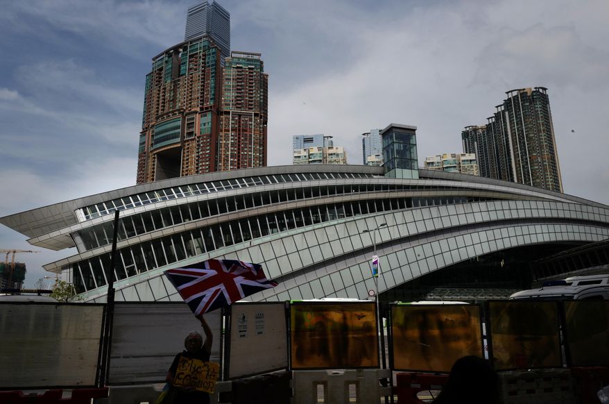 FILE - In this Sept. 22, 2018, file photo, a woman waves a British flag outside the Western Kowloon Station during a protest against the opening ceremony of the Hong Kong Express Rail Link in Hong Kong. Protesters in Hong Kong have chosen the new high-speed railway station that connects the city with mainland China as the destination for their latest march to protect the freedoms of the semi-autonomous Chinese territory. (AP Photo/Vincent Yu, File)