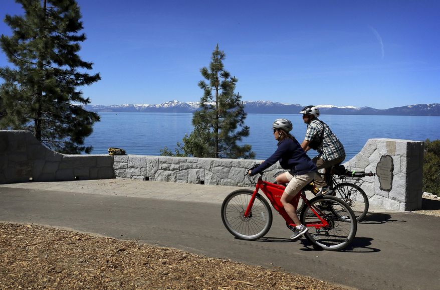 In this June 25, 2019 photo, the Tahoe Fund's CEO Amy Berry, left, and The Reno Gazette-Journal reporter Ben Spillman take a ride on the new Tahoe East Shore Trail near Incline Village, Nev. The Tahoe East Shore Trail that opened Friday (June 28) includes an 810-foot (246-meter) long bridge overhanging the lakeshore between Incline Village and a state park at Sand Harbor. (Jason Bean/The Reno Gazette-Journal via AP)