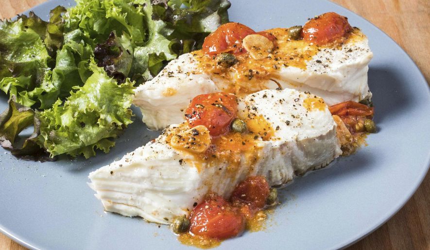 This undated photo provided by America's Test Kitchen in June 2019 shows Halibut with Roasted Garlic and Cherry Tomatoes in Brookline, Mass. This recipe appears in the book "Cook It In Your Dutch Oven." (Carl Tremblay/America's Test Kitchen via AP)