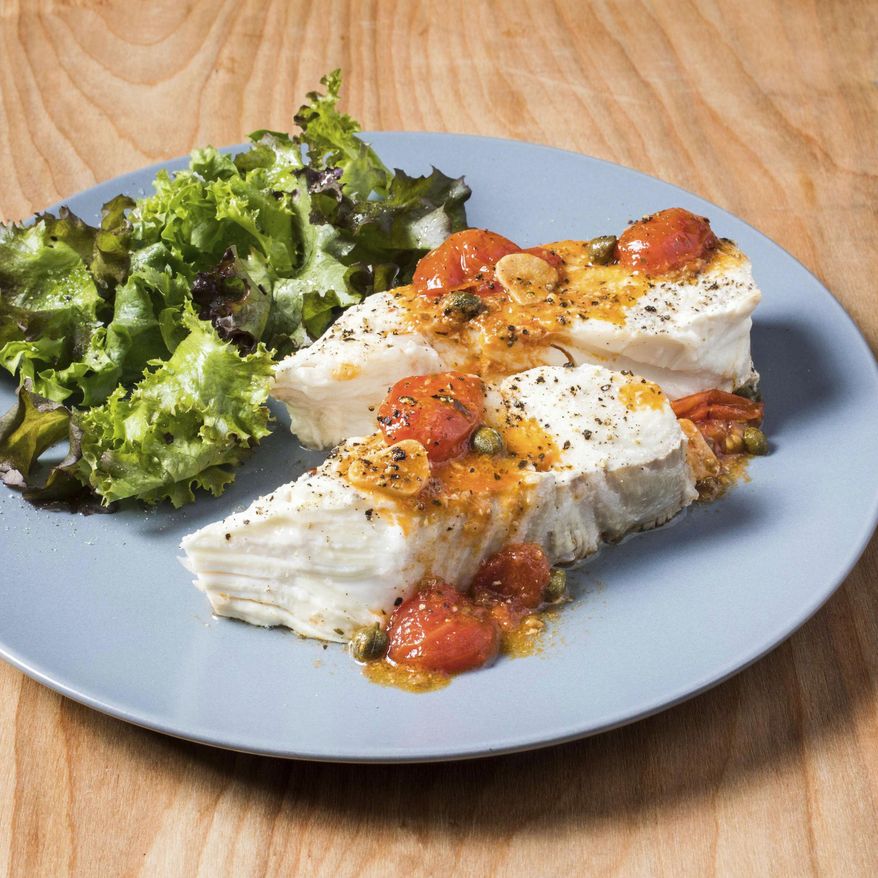This undated photo provided by America's Test Kitchen in June 2019 shows Halibut with Roasted Garlic and Cherry Tomatoes in Brookline, Mass. This recipe appears in the book "Cook It In Your Dutch Oven." (Carl Tremblay/America's Test Kitchen via AP)