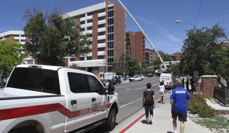People walk past a dormitory at the University of Nevada, Reno, as work crews with a crane examine damage from a July 5 explosion, in Reno, Nev., Tuesday, July 9, 2019. Nevada's state fire marshal says a small explosion in a basement boiler at the university dormitory caused a natural gas leak that triggered a much larger blast last week, severely damaging two dorms and injuring eight people. (AP Photo/Scott Sonner)