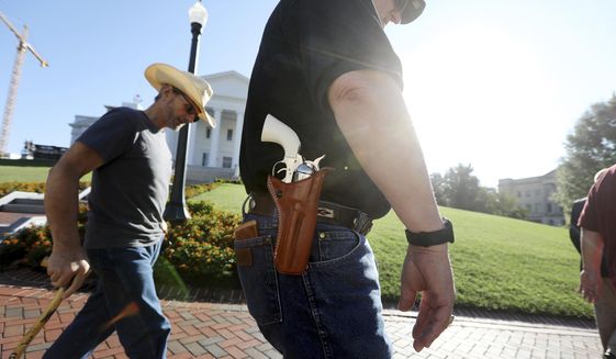 Gun rights supporters walk by the Capitol building in Richmond, Va., on Tuesday, July 9, 2019, the opening for the special session called by Virginia Gov. Ralph Northam. (Steve Earley/The Virginian-Pilot via AP) ** FILE **