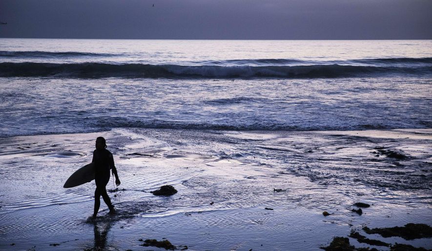 FILE - In this July 2, 2019, file photo a surfer walks out of the water after riding waves at dusk at Scripps Beach in San Diego. With hotel and airline loyalty programs, you can take the sting out of this year’s travel costs by leveraging those expenditures to pay for next year’s trip. (AP Photo/David Goldman, File)