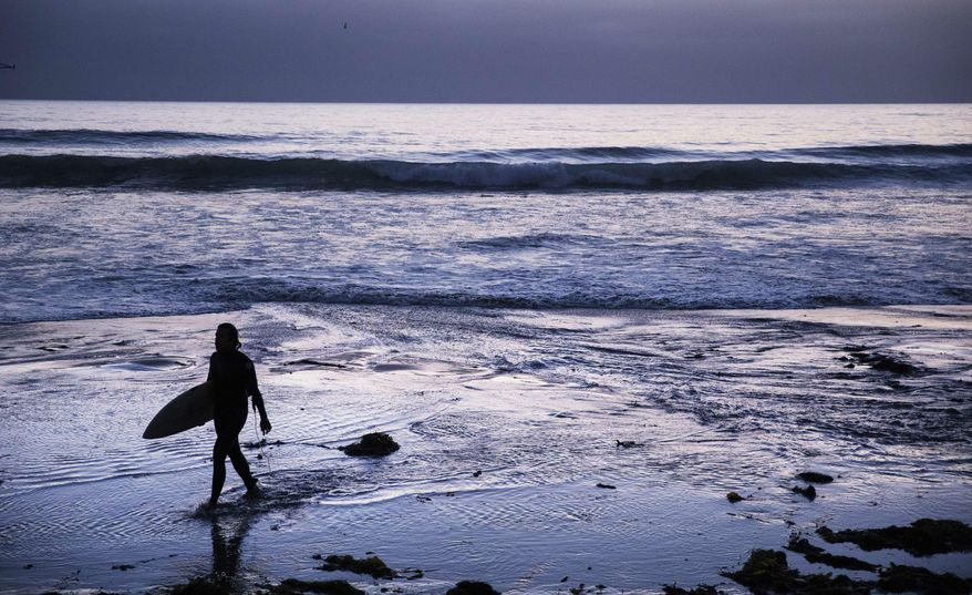 FILE - In this July 2, 2019, file photo a surfer walks out of the water after riding waves at dusk at Scripps Beach in San Diego. With hotel and airline loyalty programs, you can take the sting out of this year’s travel costs by leveraging those expenditures to pay for next year’s trip. (AP Photo/David Goldman, File)