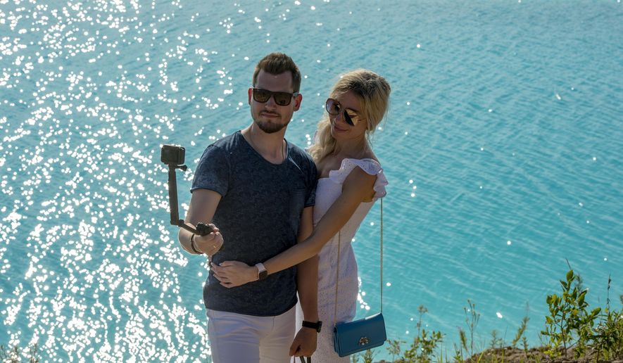 In this Friday, July 12, 2019 photo, a couple take a selfie by a lake in the Siberian city of Novosibirsk, about 2,800 kilometers (1,750 miles) east of Moscow, Russia. Thousands of Novosibirsk residents, from scantily clad women to newlyweds have been instagramming selfies near the lake nicknamed the “Siberian Malvides” after the far-flung tropical islands in the Indian Ocean. This is in fact is a man-made dumb of coal from a nearby power station that provides for most of Novosibirsk’s energy needs. (AP Photo/Ilnar Salakhiev)