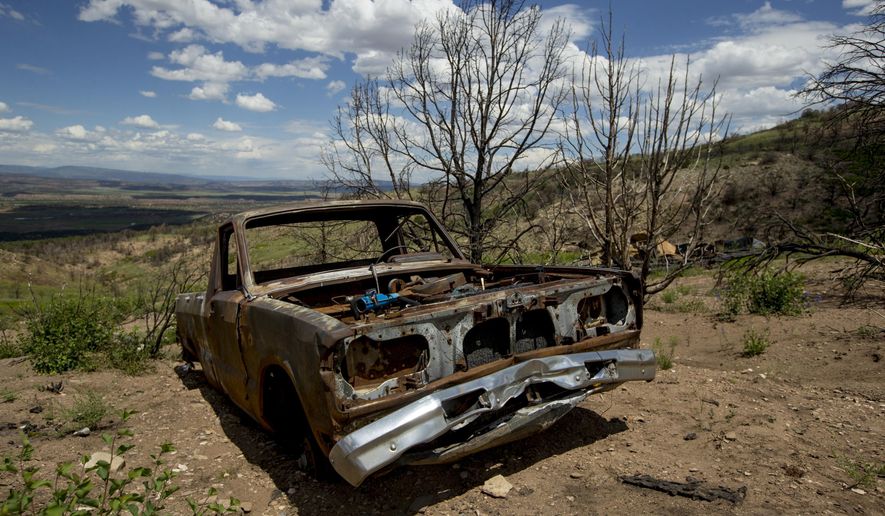In this Monday, July 8, 2019 photo, a burned pickup truck remains beside where a mobile home once stood during a tour to examine conditions near the Wildcat Wildlife Management Area roughly a year after a wildfire in Duchesne County, Utah. The Daily Herald reports that grasses and flowers are returning to the area alongside charred trees. Other vegetation, like trees and sagebrush, are expected to take longer. (Isaac Hale/The Daily Herald via AP)