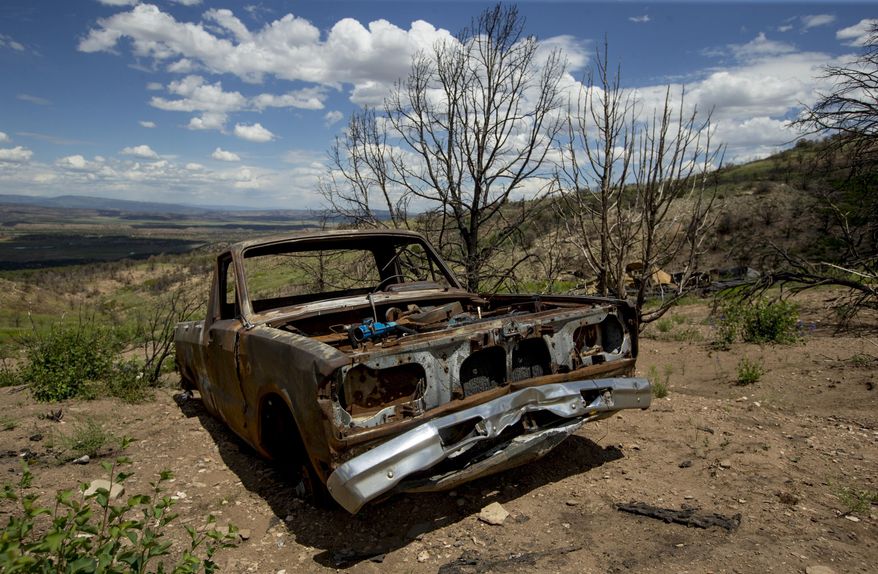 In this Monday, July 8, 2019 photo, a burned pickup truck remains beside where a mobile home once stood during a tour to examine conditions near the Wildcat Wildlife Management Area roughly a year after a wildfire in Duchesne County, Utah. The Daily Herald reports that grasses and flowers are returning to the area alongside charred trees. Other vegetation, like trees and sagebrush, are expected to take longer. (Isaac Hale/The Daily Herald via AP)