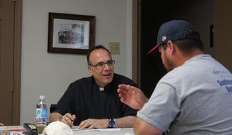 Father Jim Sichko, left, a Lexington priest, pays the electric bill of an out-of-work coal miner at Holy Trinity Catholic Church in Harlan, Kentucky, on Monday, July 15, 2019. Sichko handed out more than $20,000 on Monday to miners who are struggling to pay bills after the coal company they work for filed for bankruptcy protection. (Will Wright/Lexington Herald-Leader via AP)
