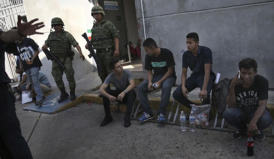 Migrants wait under guard at an immigration center on the International Bridge 1, as an immigration agent attempts to block the camera, in Nuevo Laredo, Mexico, Tuesday, July 16, 2019. A U.S. policy to make asylum seekers wait in Mexico while their cases wind through clogged U.S. immigration courts has also expanded to the violent city of Nuevo Laredo. The group was returned from the U.S. after being detained. (AP Photo/Marco Ugarte)