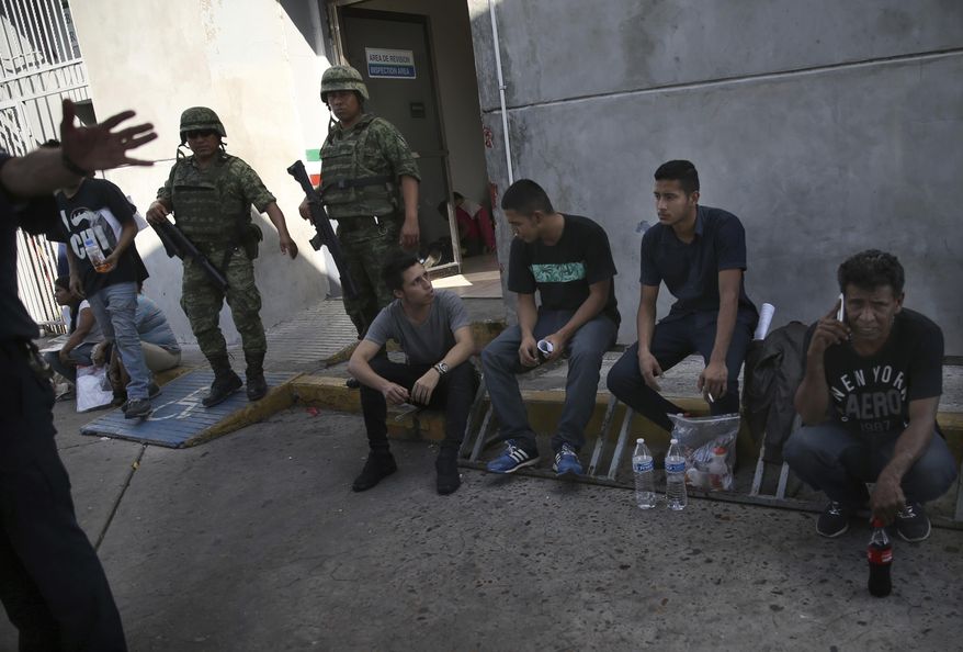 Migrants wait under guard at an immigration center on the International Bridge 1, as an immigration agent attempts to block the camera, in Nuevo Laredo, Mexico, Tuesday, July 16, 2019. A U.S. policy to make asylum seekers wait in Mexico while their cases wind through clogged U.S. immigration courts has also expanded to the violent city of Nuevo Laredo. The group was returned from the U.S. after being detained. (AP Photo/Marco Ugarte)