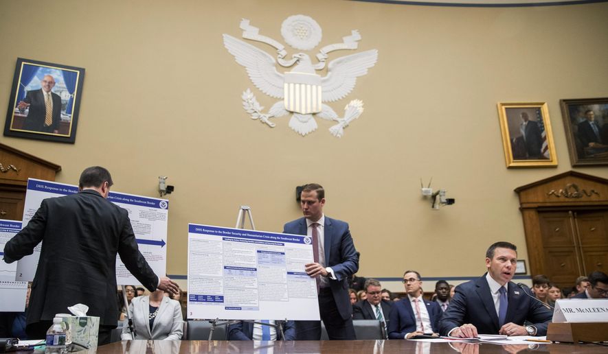 Aids set up posters as Acting Secretary of Homeland Security Kevin McAleenan, right, speaks at a House Committee on Oversight and Reform hearing on Capitol Hill in Washington, Thursday, July 18, 2019. (AP Photo/Andrew Harnik)