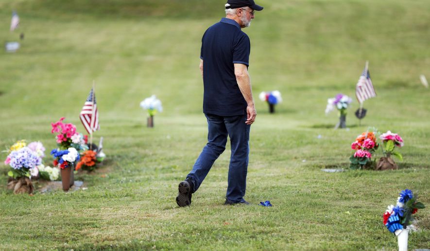 Eddie Davis walks past tributes on his way to his son Jeremy's gravestone, who died from the abuse of opioids, Wednesday, July 17, 2019, in Coalton, Ohio. Newly released prescription opioid statistics underscore how widespread pill use has been in towns and small cities of America’s Appalachian region. In Jackson County, an average yearly total of 107 opioid pills for every resident were distributed over a seven-year period. (AP Photo/John Minchillo)