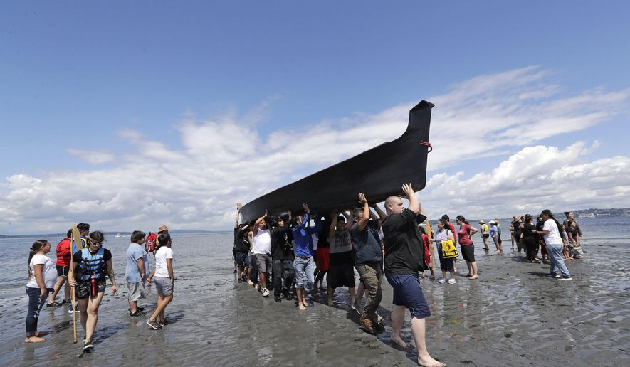 Canoe pullers and volunteers heft a canoe up the beach during a stop on the annual tribal canoe journey through the Salish Sea Thursday, July 18, 2019, in Seattle. About 20 canoes from Northwest Native coastal tribes landed Thursday at Alki Beach on one of several legs of the canoe journey that gathers other canoe families from host tribes as they travel to a final landing, this year near Bellingham, Wash., at the Lummi Nation. (AP Photo/Elaine Thompson)
