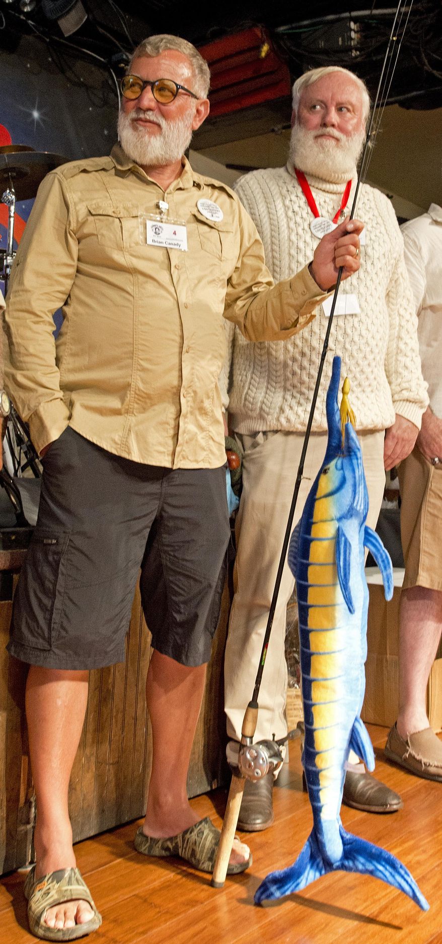 In this photo provided by the Florida Keys News Bureau, Brian Canady, left, holds a fishing rod with a faux blue marlin as he and Michael Bull, right, of Perth, Australia, endeavor to impress the judges at the Hemingway Look-Alike Contest at Sloppy Joe's Bar Thursday, July 18, 2019, in Key West, Fla. The competition, that has attracted about 135 entrants, is part of the island city's annual Hemingway Days festival that pays homage to Ernest Hemingway who lived and wrote in Key West in the 1930s. (Andy Newman/Florida Keys News Bureau via AP)