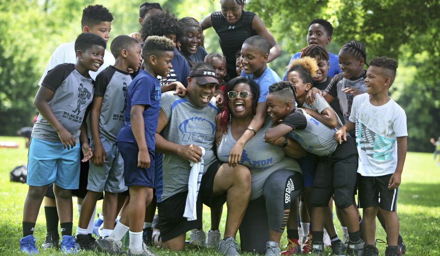 In a June 29, 2019 photo, during a break in an afternoon football practice, Michael and Maree Whitlow are showered with hugs by the kids in their Inspring Children to Excellence program. The couple felt like they had lost of their own children when 14-year-old Jaykwon Sharp was shot and killed; he had been part of the Columbus Inspiring Children to Excellence football program that the Whitow&#x27;s founded.  (Doral Chenoweth III/The Columbus Dispatch via AP)
