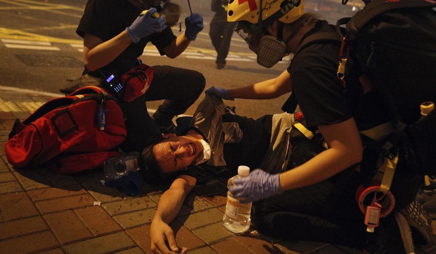 Medical workers help a protester in pain from tear gas fired by policemen on a street in Hong Kong, Sunday, July 21, 2019. Hong Kong police have thrown tear gas canisters at protesters after they refused to disperse. Hundreds of thousands of people took part in a march Sunday to call for direct elections and an independent investigation into police tactics used during earlier pro-democracy demonstrations. Police waved a black warning flag Sunday night before lobbing the canisters into a crowd of protesters. (AP Photo/Bobby Yip)