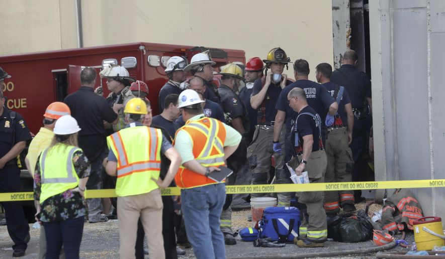 Toledo Fire and Rescue personnel stand outside an Andersons grain storage tank where two workers died after they were trapped in a silo filled with grain, Friday, July 19, 2019 in Toledo, Ohio. The workers became trapped Friday morning inside the silo operated by The Andersons. (Dave Zapotosky /The Blade via AP)