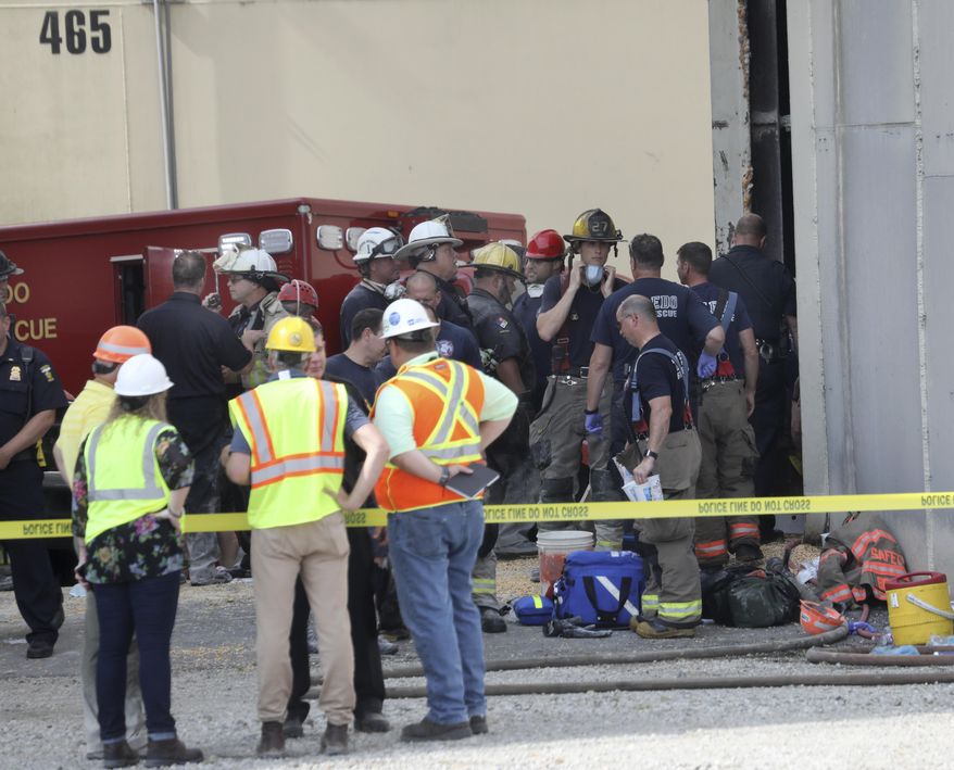 Toledo Fire and Rescue personnel stand outside an Andersons grain storage tank where two workers died after they were trapped in a silo filled with grain, Friday, July 19, 2019 in Toledo, Ohio. The workers became trapped Friday morning inside the silo operated by The Andersons. (Dave Zapotosky /The Blade via AP)