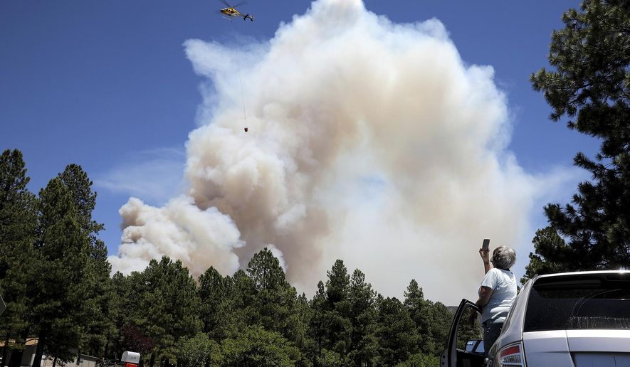 A helicopter carries a bucket of water to attack hot spots on the Museum Fire in Flagstaff, Ariz., Sunday,  July 21 2019. (Jake Bacon/Arizona Daily Sun via AP)