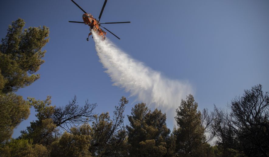 A firefighting helicopter drops water onto a wildfire in the town of Rafina, near Athens, on Tuesday, July 23, 2019. A forest fire outside Athens is threatening homes on the anniversary of a deadly blaze in the same area that claimed more than 100 lives. (AP Photo/Petros Giannakouris)