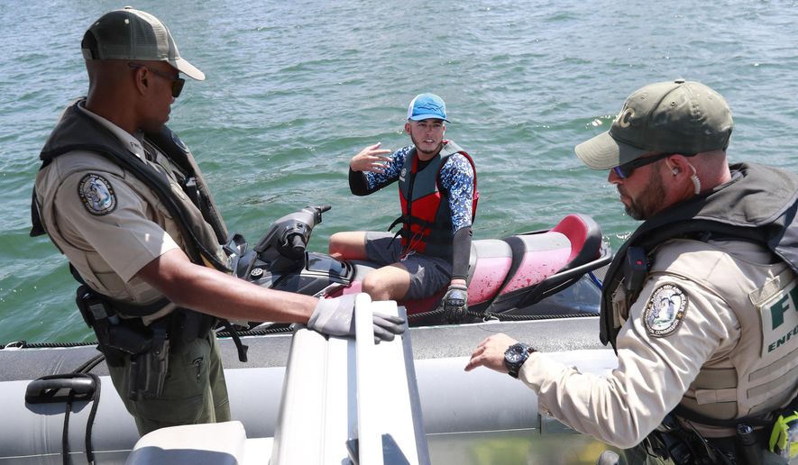 Florida Fish and Wildlife Conservation Commission officers Ronald Washington, left, and Guillermo Cartaya, right, question a boater during the first day of the spiny lobster mini-season, Wednesday, July 24, 2019, off of Miami Beach, Fla. A saltwater fishing license and a lobster stamp are required to take the crustaceans. (AP Photo/Wilfredo Lee) **FILE**