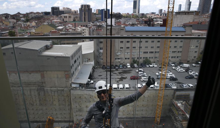 A window cleaner waves as he takes a break from repelling down the side of a high-rise building in Istanbul, Monday, July 15, 2019. (AP Photo/Lefteris Pitarakis)