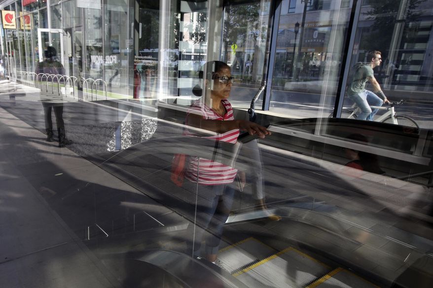 In this Monday, July 15, 2019 photo a passer-by, center, uses an escalator while emerging from a subway station, in Boston's Seaport district. On Friday, July 26, the Commerce Department issues the first estimate of how the U.S. economy performed in the April-June quarter. (AP Photo/Steven Senne)