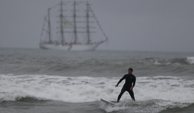 A surfer slides off a dying wave as he surfs in front of the BUP Union naval teaching ship, which was carrying the Pan Am Games torch, off the coast of Lima, Peru, Friday, July 26, 2019. In the Peruvian capital, where dozens of schools teach locals and tourists from around the world how to ride the waves at beaches with Hawaiian names, professional surfers from across the Americas are preparing to compete when the sport is featured for the first time in the Pan Am Games.(AP Photo/Rebecca Blackwell)