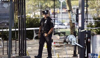 A police officer walks by yellow evidence markers at a playground in the Brownsville neighborhood in the Brooklyn borough of New York, Sunday, July 28, 2019. Police said, one man was killed and at least 11 others were injured in a shooting late Saturday night at the park. (AP Photo/Mark Lennihan)