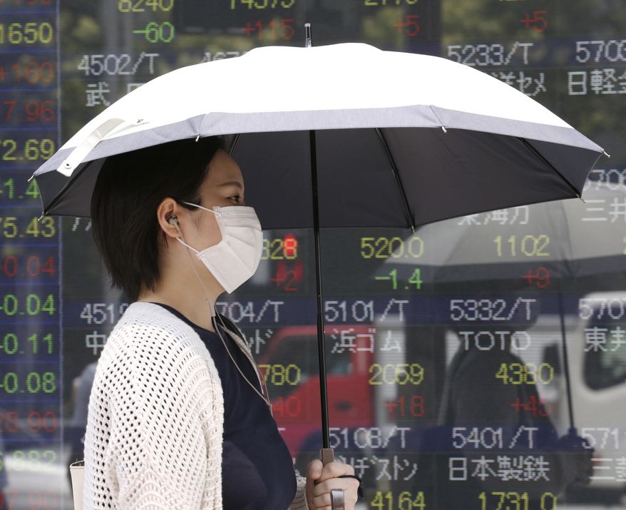 A woman walks by an electronic stock board of a securities firm in Tokyo, Tuesday, July 30, 2019. Shares were mostly higher in Asia on Tuesday as envoys from the U.S. and China prepared to resume trade talks, this time in Shanghai. (AP Photo/Koji Sasahara)