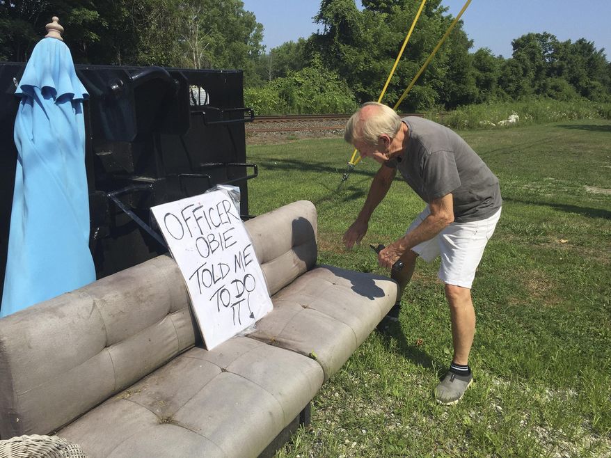 In this July 30, 2019 photo, Guthrie Center director George Laye searches for clues that might identify the person who dumped an old couch and other refuse in front of the nonprofit's construction bin in Great Barrington, Mass. Whoever dumped the trash at the building made famous in Arlo Guthrie's 1965 Thanksgiving anthem "Alice's Restaurant Massacree" has a sense of humor. That person had filled the dumpster with trash and left a grubby sofa nearby, along with a sign that said: "Officer Obie told me to do it." (Heather Bellow/The Berkshire Eagle via AP)