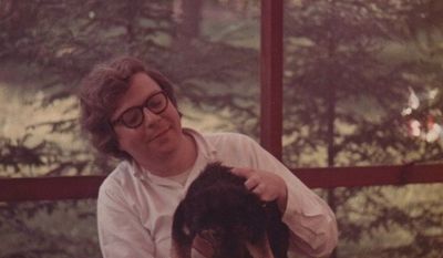 A young, smiling, shaggy-haired Bill Schulz sitting on my family&#39;s back porch in Carmel, New York. In his lap is the scruffy family dog named Lady Muttley.
