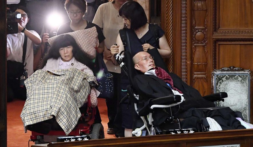 Two newly-elected lawmakers, Yasuhiko Funago, right, and Eiko Kimura, in wheelchairs are helped to arrive for an extraordinary session of the parliament's upper house in Tokyo Thursday, Aug. 1, 2019. Japan’s parliament convened after elections and a minor renovation at the upper house. Funago, who has Amyotrophic Lateral Sclerosis, a progressive neurological disease known as ALS, and Kimura who has cerebral palsy, won the July 21 elections at the less-powerful of the two chambers, representing an opposition group. (Muneyuki Tomari/Kyodo News via AP)