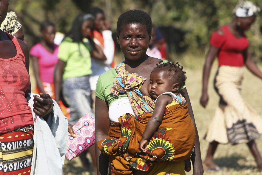 A woman with her baby waits for Mozambique President Filipe Nyusi and Renamo leader Ossufo Momade to arrive for a peace accord signing ceremony at Gorongosa National Park, about 170 kilometres from Beira, Mozambique, Thursday, Aug, 1, 2019. The peace agreement is set to bring an end to decades of hostilities that included a 15 year civil war. The former rebel groups remaining fighters are disarming just weeks before a visit by Pope Francis and a national election that will test the now-political rivals new resolve. (AP Photo/Tsvangirayi Mukwazhi)