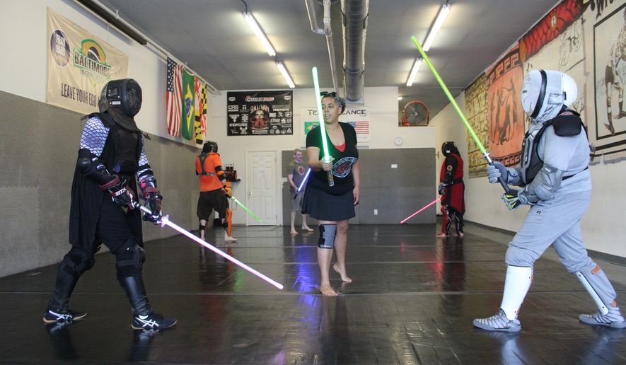 Jessica Newing (center, green saber) prepares to officiate a practice round between Jay Madan (left, purple saber) and Clint Darby (right, yellow saber) at a meeting of The Saber Legion&#39;s Maryland chapter in Essex, Md., on June 30, 2019. (Photo by Adam Zielonka / The Washington Times)