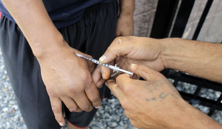 FILE - In this Wednesday, Aug. 23, 2017 file photo an unidentified heroin user, left, is injected by another man, right, on the street near a strip of land sometimes referred to as "Methadone Mile," in Boston. Fatal drug overdoses in the U.S. were long known as being most common in big cities. That changed 13 years ago, when Appalachia and other rural areas started seeing the nation’s highest overdose death rates. According to a government report released on Friday, Aug. 2, 2019, it’s shifted back again. (AP Photo/Steven Senne)