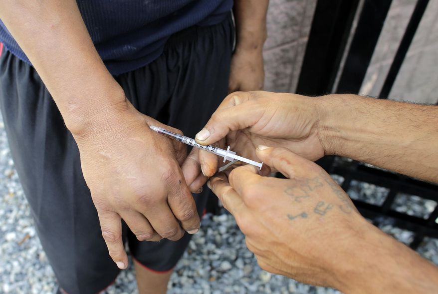 FILE - In this Wednesday, Aug. 23, 2017 file photo an unidentified heroin user, left, is injected by another man, right, on the street near a strip of land sometimes referred to as "Methadone Mile," in Boston. Fatal drug overdoses in the U.S. were long known as being most common in big cities. That changed 13 years ago, when Appalachia and other rural areas started seeing the nation’s highest overdose death rates. According to a government report released on Friday, Aug. 2, 2019, it’s shifted back again. (AP Photo/Steven Senne)