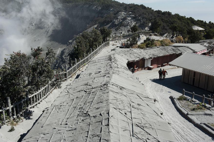 In this Saturday, July 27, 2019, file photo, members of the National Search and Rescue Agency walk among buildings covered in volcanic ash from the eruption of Mount Tangkuban Perahu in Subang, West Java, Indonesia, Saturday, July 27, 2019. The volcano erupted Friday forcing tourists and residents to flee the mountain. (AP Photo/Kusumadireza, File)