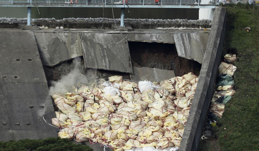 A bag of aggregate, a mixture of sand, gravel and stone, is thrown onto the damaged Toddbrook Reservoir near the village of Whaley Bridge,in Derbyshire, England, Saturday, Aug. 3, 2019. Emergency workers are racing to lower water levels behind a damaged dam in northwest England as forecasters warn more bad weather is on the way. Pumps have reduced the water level in Toddbrook Reservoir by half a meter (20 inches) since Thursday, but authorities warn that pressure on the 180-year-old dam remains severe. (Yui Mok/PA via AP)