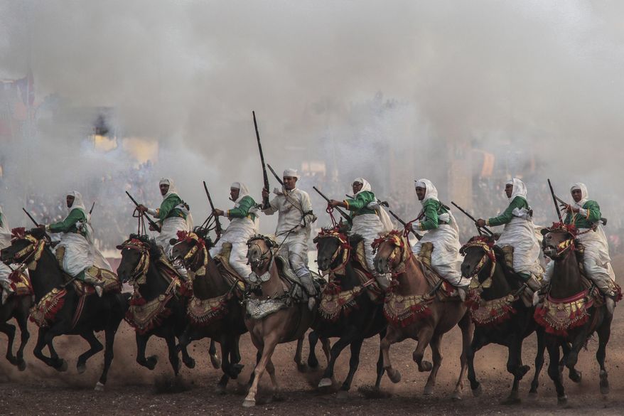In this Thursday, July 25, 2019 photo, a troupe charges firing their rifles during Tabourida, a traditional horse riding show also known as Fantasia, in the coastal town of El Jadida, Morocco. Thousands of visitors descend on the Moroccan coastal city of El Jadida each July to attend the largest equestrian show in the kingdom _ a breathtaking horseback performance that combines synchronized riding with decorative guns. (AP Photo/Mosa'ab Elshamy)