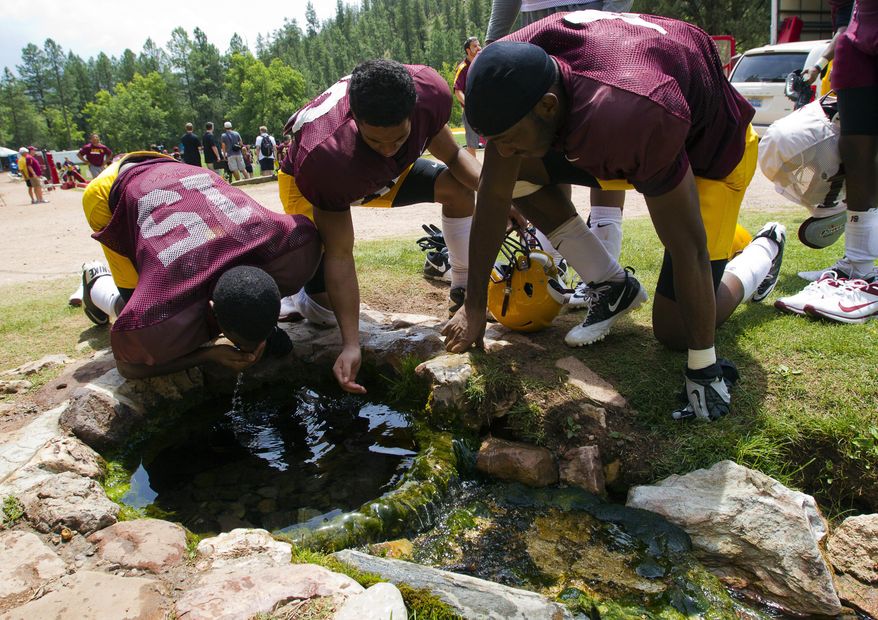 FILE - In this Aug. 15, 2012, file photo, Arizona State wide receivers Rashad Ross, left, JJ Holliday, center, and Alonzo Agwuenu drink water from a spring after NCAA college football practice at Camp Tontozona in Kohls Ranch, Ariz. Arizona State football players are returning to a newly renovated training camp, restoring a beloved football tradition. The Arizona Republic reported Monday, Aug. 5, 2019, that the Sun Devils had to cancel the preseason training camp last year at their usual facility near the mountain town of Payson after wet conditions delayed the installation of an artificial grass football field. The field was completed in April at Tonto Creek Camp, which was formerly named Camp Tontozona. (Michael Chow/The Arizona Republic via AP, File)